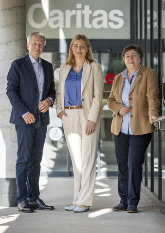 Das Direktorium der Caritas Steiermark steht vorm Eingang der Zentrale und lächelt in die Kamera